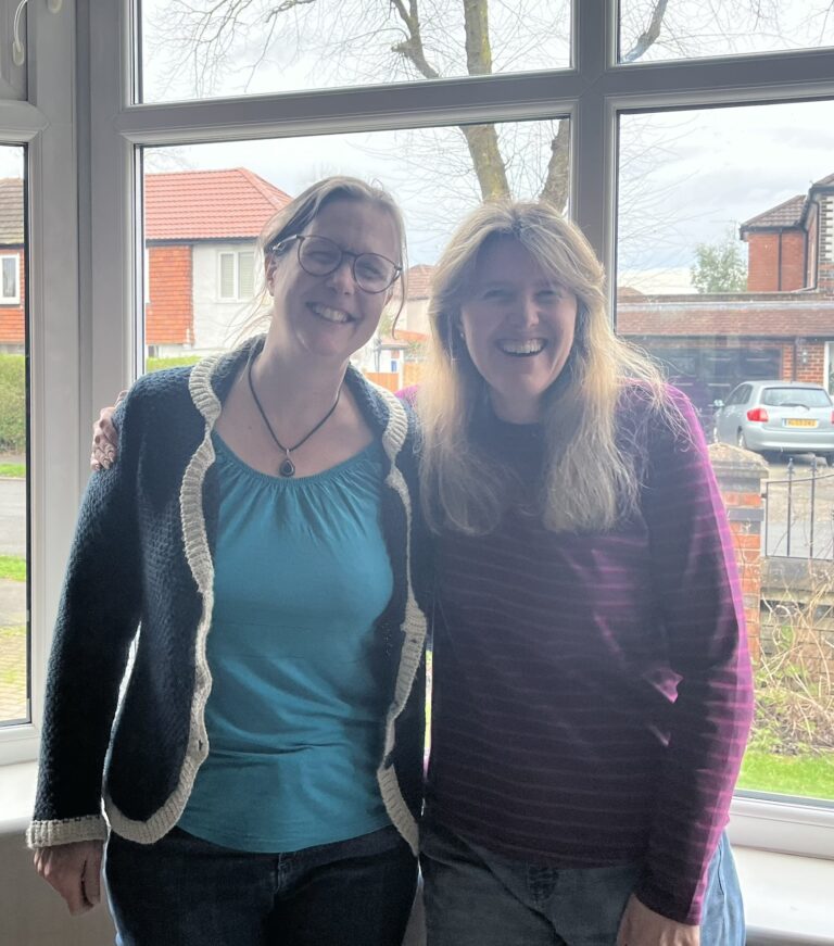 Book talk with Lisa. Image shows Jane Eggers and Lisa de Caux in front of a living-room window. They're both smiling at the camera.