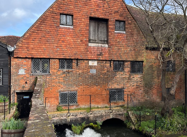 View of Winchester City Mill, an old, red-brick building with water gushing out from underneath