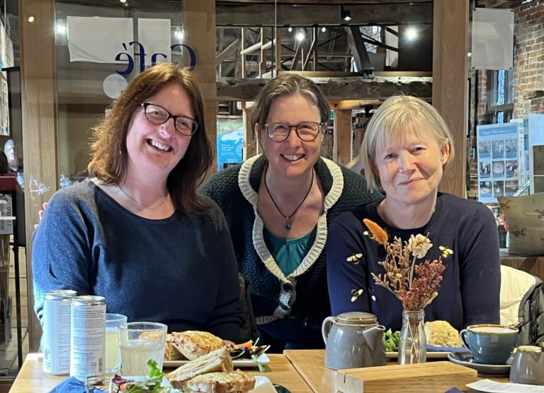 Laura Massey, Jane Eggers and Katherine Ledger, seated at a table with drinks and plates of food