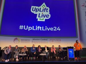 A panel of people are seated on stage. On the huge screen behind them it says, 'UpLift Live', with the hashtag #UpLiftLive24.