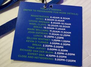 Blue lanyard and a blue name label with the back facing up. It lists all the sessions and their timings.