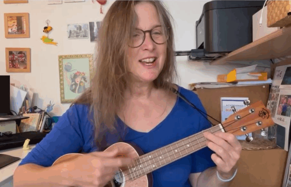 Woman in a blue top playing the ukulele and singing
